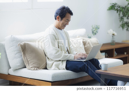Middle-aged man using a laptop in the living room Middle-aged man using a laptop in the living room 117716951