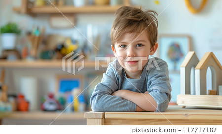 A boy sitting at a wooden table with his arms folded and looking at the camera A boy sitting at a wooden table with his arms folded and looking at the camera 117717182