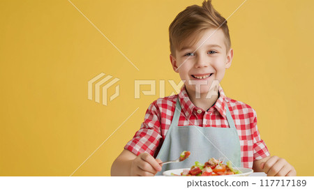 A boy wearing an apron eating food on a yellow background 117717189