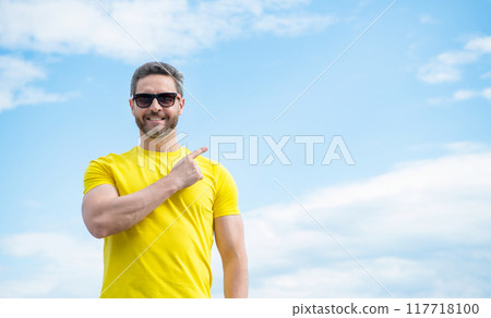 happy man in yellow shirt and sunglasses point finger on on sky background 117718100