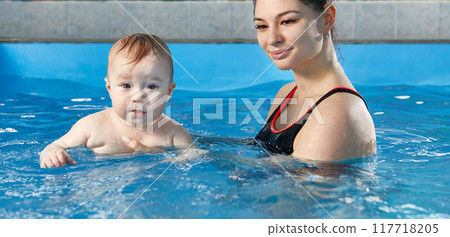 Little baby learning to swim in pool with teacher 117718205