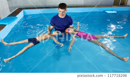 Little children learning how to swim in pool with teacher, laying on he back 117718206