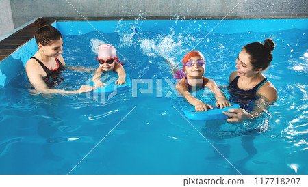 Little girl learning to swim in indoor pool with pool board and trainer 117718207