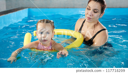 Preschool girllearning to swim in pool with foam noodle with young trainer Preschool girllearning to swim in pool with foam noodle with young trainer 117718209
