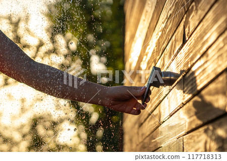Female hand turns outdoor shower faucet at sunset. Concept of summer fun and refreshing shower with flowing water Female hand turns outdoor shower faucet at sunset. Concept of summer fun and refreshing shower with flowing water 117718313
