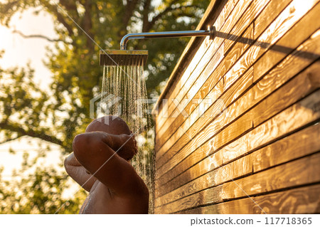 Man enjoying refreshing outdoor shower at sunset. Concept of relaxation and natural bathing 117718365