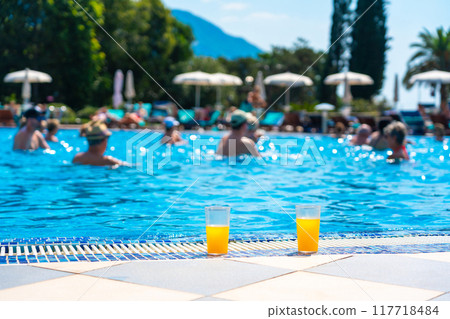 Glass of fresh cool orange juice drink next to swimming pool Glass of fresh cool orange juice drink next to swimming pool 117718484