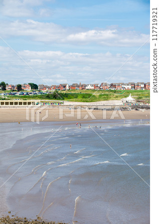 人們在南威爾斯郊區的淺沙灘上放鬆，遠處山上有一排紅磚房 117719321