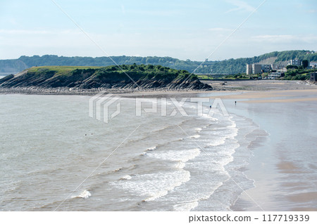 A shallow sandy beach with white waves and a rocky hill in the suburbs of South Wales 117719339