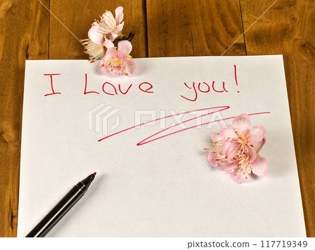 On a wooden surface lies a sheet of white paper written in red felt-tip text "I love you!" and decorated with artificial flowers. On a wooden surface lies a sheet of white paper written in red felt-tip text "I love you!" and decorated with artificial flowers. 117719349