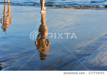Reflections of the two female figures in the wet coast. Two female figures are reflected in the wet sand prebrezhnogo Reflections of the two female figures in the wet coast. Two female figures are reflected in the wet sand prebrezhnogo 117719355