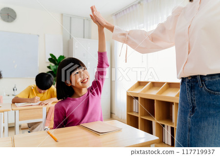Joyful Asian primary student celebrating achievement with teacher through energetic high-five Joyful Asian primary student celebrating achievement with teacher through energetic high-five 117719937