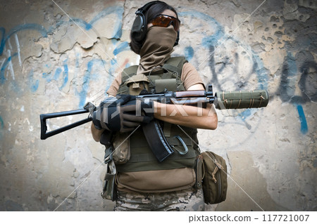 A young brave girl in a military uniform holds a weapon in her hands. 117721007