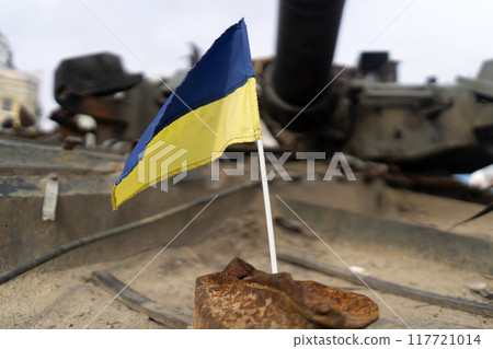 Ukrainian flag on the background of destroyed military equipment 117721014