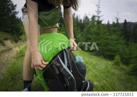 A travelling girl, woman puts a rain cover on her backpack. 117721031