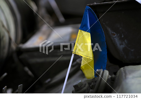 Ukrainian flag on the background of destroyed military equipment Ukrainian flag on the background of destroyed military equipment 117721034