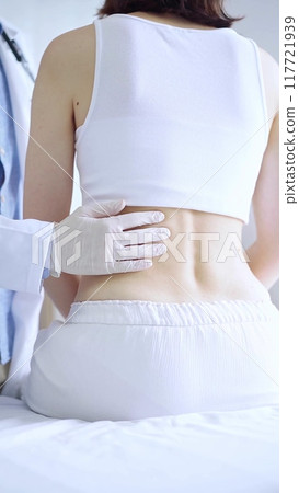 Doctor and patient. Physician wearing white medical gloves examining back of female patient in clinic. Orthopedics and pediatric in medicine Doctor and patient. Physician wearing white medical gloves examining back of female patient in clinic. Orthopedics and pediatric in medicine 117721939