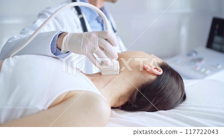 Doctor man is using ultrasound equipment on neck of female patient lying down for a medical examination. Medicine and science 117722043