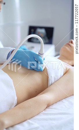 Doctor man wearing blue protective gloves is using ultrasound equipment on the breast of a female patient. Mammary gland health Doctor man wearing blue protective gloves is using ultrasound equipment on the breast of a female patient. Mammary gland health 117722057
