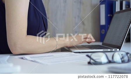 Woman with dark blue blues is working from home office typing on laptop computer keyboard. Business concept 117722078