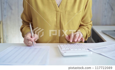 Businesswoman with yellow blues is using white calculator and taking notes in her office. Taxes and audit concept 117722089