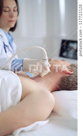 Doctor performing neck ultrasound exam on male patient 117722128