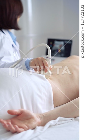 Doctor performing ultrasound examination on patient's back 117722132