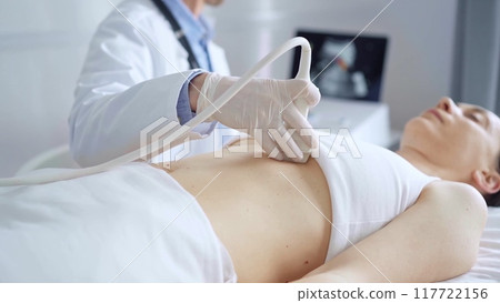 Doctor man, wearing white medical gloves, is using ultrasound equipment on the breast of a female patient lying down for a medical cardiology examination. Medicine concept 117722156