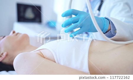 Doctor man, wearing blue medical gloves, is using ultrasound machine to examine internal organs of a patient woman, close up vie. Female mammary gland health. Medicine Doctor man, wearing blue medical gloves, is using ultrasound machine to examine internal organs of a patient woman, close up vie. Female mammary gland health. Medicine 117722162