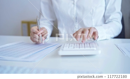 Businesswoman with white blues calculating finance with calculator and taking notes at office table. Audit and taxes 117722180