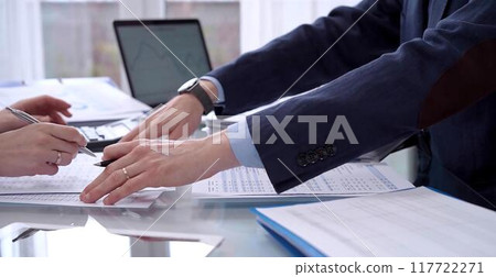 Business people wearing blue suits are reviewing financial data in office. Two professionals analyzing paper reports using calculators. Audit and taxes concept 117722271