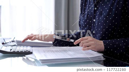 Businesswoman using calculator and reviewing ring folder of financial documents with magnifying glass at desk in modern office. Audit and taxes in business 117722280