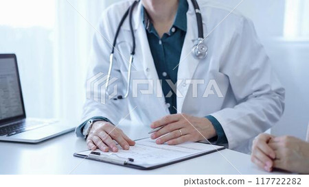 Doctor and a patient. The physician, wearing a white medical coat over a green shirt, is gesturing with his hands during a consultation in the clinic. Medicine 117722282