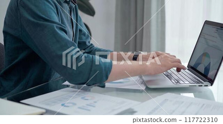 Entrepreneur wearing green shirt is working at laptop with data analysis charts. Businessman analyzing statistical data. Business concept 117722310