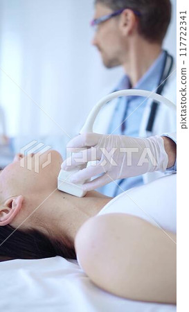 Doctor man wearing white protective gloves is using ultrasound machine to examine neck of female patient in hospital. Medicine, thyroid gland health Doctor man wearing white protective gloves is using ultrasound machine to examine neck of female patient in hospital. Medicine, thyroid gland health 117722341