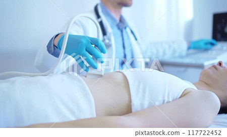 Doctor man wearing a blue medical gloves using an ultrasound equipment on a female patient lying down in clinic cabinet. Medicine concept 117722452