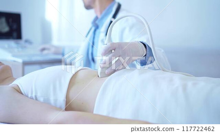Doctor man wearing a blue medical gloves using an ultrasound equipment on a female patient lying down in clinic cabinet. Medicine concept 117722462