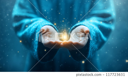 A pair of hands gently cradling a glowing golden light 117723631