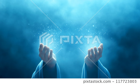 Outstretched hands emitting glowing particles of light in a mystical, foggy blue atmosphere Outstretched hands emitting glowing particles of light in a mystical, foggy blue atmosphere 117723803