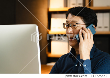A middle-aged man making a phone call at a computer A middle-aged man making a phone call at a computer 117725442