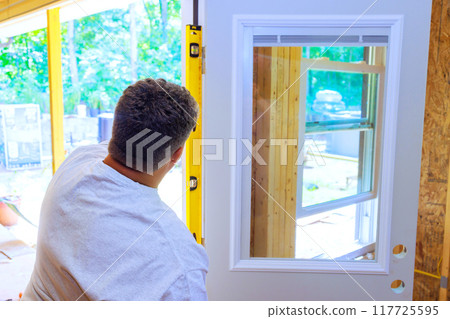 Installing front door of new house, carpenter uses yellow spirit measure level Installing front door of new house, carpenter uses yellow spirit measure level 117725595