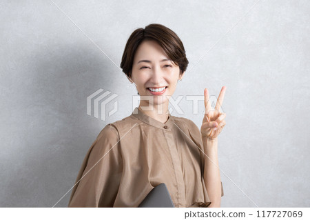 A woman looking at the camera making a peace sign while holding a laptop 117727069