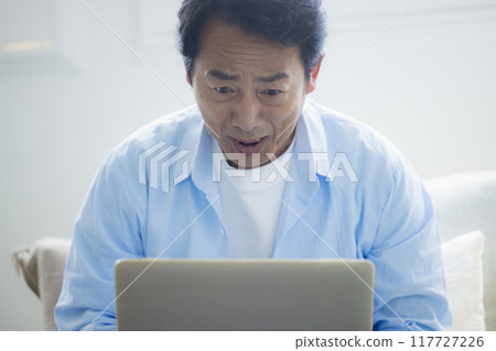 Middle-aged man using a laptop in the living room Middle-aged man using a laptop in the living room 117727226