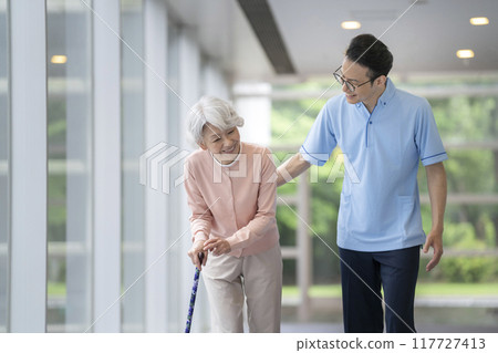 Senior woman walking with a cane and care staff 117727413