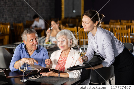 Waitress serving wine to guests perusing menu in restaurant 117727497