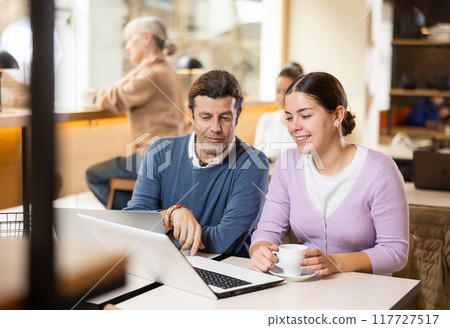 Calm caucasian man and woman sitting in cafe diligently doing their work on laptop Calm caucasian man and woman sitting in cafe diligently doing their work on laptop 117727517