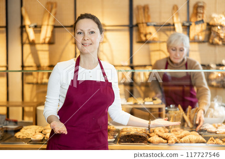 Cheerful female baker welcoming everyone into her bakery Cheerful female baker welcoming everyone into her bakery 117727546