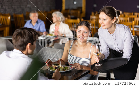 Waitress serves order of wine and wishes visitors young couple pleasant appetite and good time Waitress serves order of wine and wishes visitors young couple pleasant appetite and good time 117727663