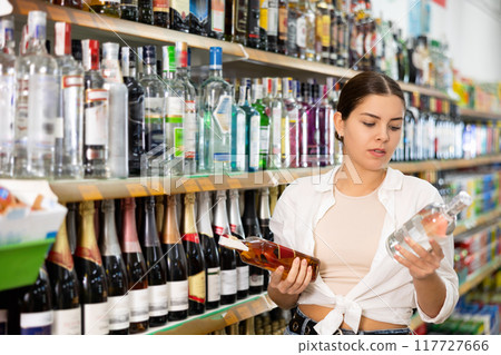 Young woman choosing bottle of liquor for herself in supermarket 117727666