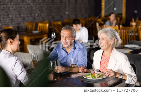 Elderly parents and adult daughter in cafe celebrate family important event occasion. 117727700
